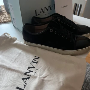 Svarta captoes från Lanvin - Snygga svarta sneakers från Lanvin med en blank tå och snörning. Skorna har en stilren design med en vit sula som kontrasterar mot det svarta. Perfekta för en trendig look. Ganska använda men fof i ett bra skick!