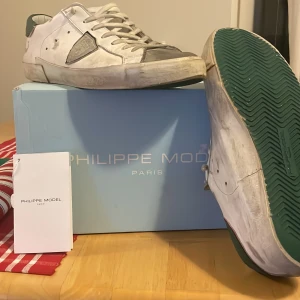 Vita sneakers från Philippe Model - Snygga vita sneakers från Philippe Model med gröna sulor och grå detaljer. Putsar man mockan och tvättar dom lite så är dom som nya. Inga defekter i skon eller utanpå. Hör gärna av er vid funderingar eller frågor (pris ej hugget i sten). Nypris: 4500kr 