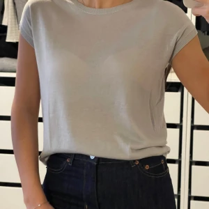 Grå kortärmad topp från Basic - Säljer en stilren grå topp från Basic. Den är kortärmad och har en rund halsringning. Perfekt för en enkel och avslappnad look. Passar bra till jeans eller kjol. Tunnt stickad 