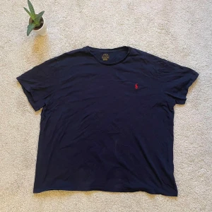Mörkblå t-shirt från Polo Ralph Lauren - Säljer en stilren mörkblå t-shirt från Polo Ralph Lauren med det klassiska röda broderade logotypen på bröstet. Perfekt för en avslappnad look. T-shirten är kortärmad och tillverkad i mjuk bomull.