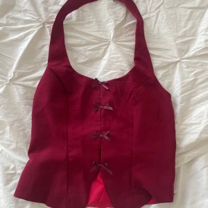 Vinröd korsettliknande topp - Snygg vinröd korsettliknande topp med rosetter framtill. Säljer då den inte passade mig!!