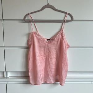 Rosa linne från Rut&Circle - Säljer ett sött rosa linne från Rut&Circle med spetsdetaljer vid halsringningen. Linnet har tunna axelband och en lätt glansig finish. Perfekt för varma dagar eller som ett lager under en kavaj.🩷