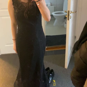 Svart långklänning - Elegant svart långklänning med glittriga detaljer. Klänningen har en figurnära passform och är ärmlös, vilket ger en stilren och sofistikerad look. Perfekt för festliga tillfällen. (Köpt i Bulgarien) (använd 1 gång)