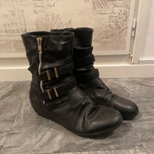 Svarta boots med dragkedja och spännen - Snygga svarta boots i skinn med dragkedja och dekorativa spännen. Insidan har ett leopardmönstrat foder. Lite slitna i fram på skorna