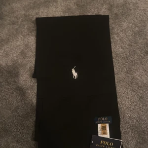 Halsduk från Polo Ralph Lauren - Snygg svart halsduk från Polo Ralph Lauren med det ikoniska logotypen broderad på framsidan. Perfekta för en stilren look.