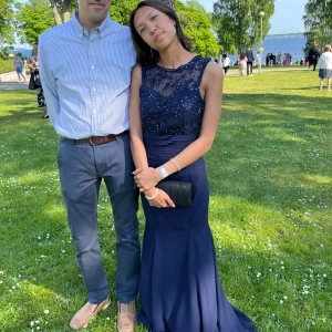 Mörkblå balklänning - Elegant mörkblå långklänning med glittrande paljettdetaljer på överdelen. Klänningen har en vacker öppen rygg och är ärmlös, vilket ger en sofistikerad look. Perfekt för speciella tillfällen. Underklänningen är uppsyd då jag är 164cm lång