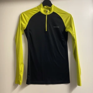 Svart och gul långärmad tröja från In Motion - Säljer en svart och gul långärmad tröja från In Motion. Tröjan har en dragkedja framtill och är perfekt för träning. Den är tillverkad i ett syntetmaterial som andas och ger en bekväm passform.