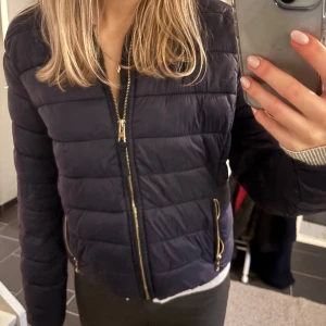 Mörkblå pufferjacka från Bershka - Snygg mörkblå pufferjacka från Bershka med dragkedja och praktiska fickor. Jackan har långa ärmar och en stilren design som passar perfekt för kyligare dagar. Perfekt för dig som vill ha en trendig och bekväm jacka.