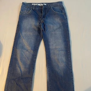 Blå jeans från Soda - Säljer ett par snygga blå jeans från märket Soda. De har en klassisk femficksdesign med två framfickor, två bakfickor med gul söm och en liten myntficka. Jeansen har en dragkedja och knapp framtill. Perfekta för vardagsbruk!