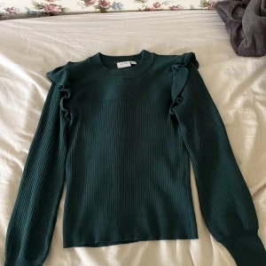 Mörkgrön ribbad tröja från VILA - Säljer en snygg mörkgrön ribbad tröja från VILA i storlek XS. Tröjan har långa ärmar och fina volangdetaljer på axlarna. Perfekt för höst och vinter! 🧡