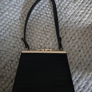 Svart väska  - En fin svart mer gammaldags väska med gulddetaljer! Bra skick! Har bara använts en gång! Väskan är på den mindre sidan! Pris kan förhandlas!