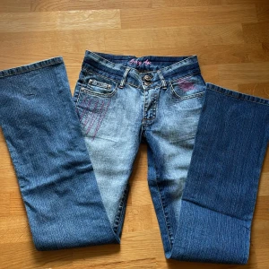 Crazy age jeans - Blå lågmidjade crazy age jeans med rosa detaljer. Midjemåttet tvärs över är 32cm och innerbenslängden är 71cm. Sista bilden är lånad från en tidigare säljare. Skriv om du har frågor eller för fler bilder🩷 