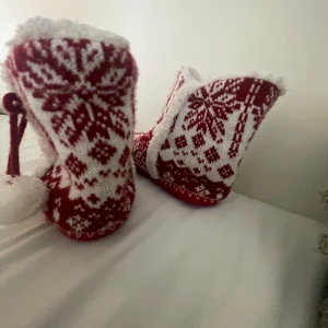 Mysiga röda och vita stickade tofflor - Säljer ett par supermysiga stickade tofflor i rött och vitt. De har ett fint mönster och är perfekta för vintern. Tofflorna har en fluffig insida och söta små bollar som hänger på sidan. Perfekta för att hålla fötterna varma under kalla dagar!
