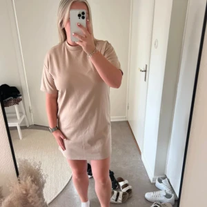 Beige t-shirtklänning - Säljer en enkel och stilren beige t-shirtklänning. Den är kortärmad och har en avslappnad passform som gör den perfekt för vardagsbruk. Klänningen är gjord av ett mjukt och bekvämt material, troligen bomull eller en bomullsblandning. Perfekt för sommardagar eller som en casual outfit.