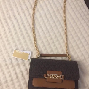 Michael Kors Heather Handväska väska - Storlek:  Höjd: 13.5 cm i storlek Längd: 23 cm i storlek Vidd: 7 cm i storlek Handtag: 53 cm i storlek Förslutning: Magnetlås Utvändigt material: Polyvinylklorid Foder: Textil Tyg:Skinnimitation Väskan är som ny endast använd 5-6 gånger  Ny pris 3700