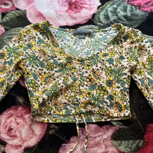 Blommig croppad topp med knytband - Säljer en superfin blommig croppad topp i storlek XS. Den har ett knytband framtill som ger en söt detalj.