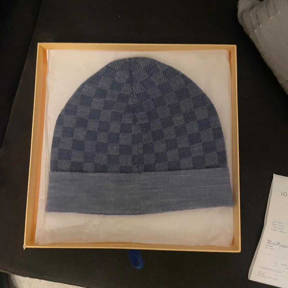 Säljer en mössa från Louis Vuitton. Den är i nytt skick och kommer i originalförpackning. Mössan har ett klassiskt rutmönster och en broderad LV-logga framtill. Perfekt för att hålla stilen i vinter!. Asusteet.