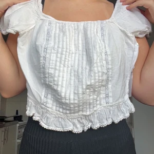 Vit blus med spetsdetaljer - Charmig vit blus med spetsdetaljer och volangkant. Den har korta puffärmar och en söt, romantisk stil. Perfekt för sommarens alla tillfällen!