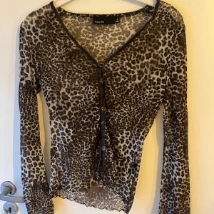 Leopardmönstrad topp från KappAhl - Snygg leopardmönstrad topp från KappAhl i storlek M. Den är gjord av 100% polyamid och har en v-ringad design med knappar framtill. Perfekt för en utekväll eller fest! Toppen har långa ärmar och är i  bra skick.