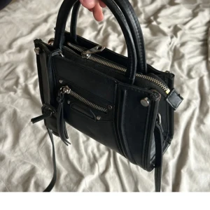 Svart handväska med dragkedja - Snygg svart handväska i skinn med flera dragkedjor och detaljer. Väl använd men äger för många väskor så nu är det dags för en ny owner 😇😇