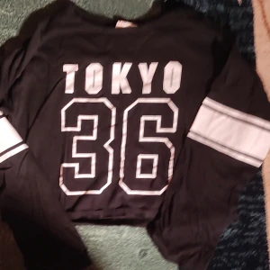 Svart t-shirt med stadstryck 2st - Cool svart t-shirt med tryck av olika städer som Tokyo, London, Berlin, Seoul, New York och LA. Den har vita ränder på ärmarna och en bred rand längst ner. Perfekt för en avslappnad stil! I denna ingår 2 t-shirts ena långarmad och den andra kort armad