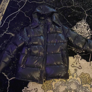 Moncler Maya - Säljer en snygg svart pufferjacka från Moncler i mycket bra skick. Jackan har en glansig finish och är perfekt för kalla dagar. Den har en dragkedja framtill och långa ärmar. Perfekt för vintern och hösten!