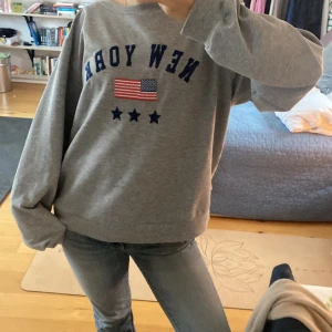 Grå sweatshirt med New York-tryck - Säljer en grå sweatshirt med texten 'NEW YORK' och en amerikansk flagga på. Den är i bra skick och superbekväm att ha på sig💕