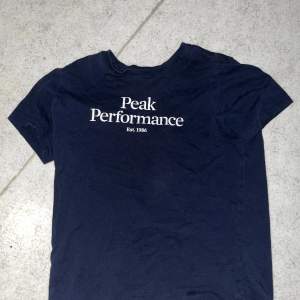 Säljer en snygg mörkblå t-shirt från Peak Performance i storlek M barn storlek. Den har en klassisk design med korta ärmar och märkesloggan tryckt på bröstet. Perfekt för vardagsbruk eller träning. Skön och stilren! 💙