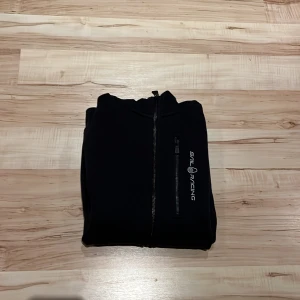 Svart hoodie från Sail Racing - Säljer en svart hoodie från Sail Racing i mycket bra skick. Den har en dragkedja framtill och en praktisk huva. Perfekt för höst och vår, och passar till vardag . Storleken är normal och materialet känns mjukt och bekvämt.