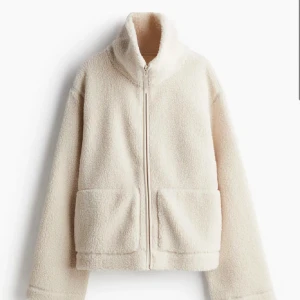 Beige teddyjacka - Mysig beige teddyjacka med dragkedja och hög krage. Perfekt för kyliga dagar när du vill vara både varm och stilren. Jackan har långa ärmar och två praktiska fickor framtill. Passar perfekt till höst- och vintergarderoben!