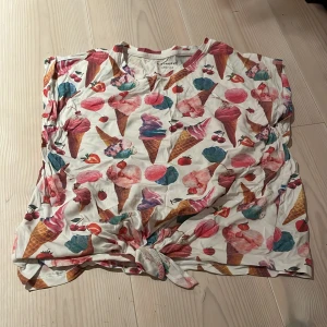 Färgglad t-shirt med glassmotiv från Firefly - Säljer en superfin och färgglad t-shirt från Firefly med ett härligt glassmotiv. Perfekt för sommardagar! T-shirten har en knytning framtill som ger en extra touch. Materialet är mjukt och bekvämt, perfekt för varma dagar. Passar både till stranden och stan! 🍦