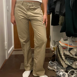 Jeanerica byxor - Säljer ett par snygga beige byxor i normal passform. De är perfekta för både vardag och lite mer uppklädda tillfällen. Byxorna har en klassisk design med knappar och dragkedja framtill. Storleken är 30/32.  De är i mycket bra skick!