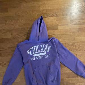 Säljer en snygg lila hoodie köpt i Chicago med texten 'Chicago' tryckt på framsidan. Den är gjord av 50% bomull och 50% polyester, vilket gör den både mjuk och hållbar.