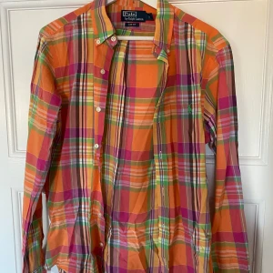 Färgglad rutig skjorta från Polo Ralph Lauren - Säljer en supercool och färgglad rutig skjorta från Polo Ralph Lauren i storlek S. Skjortan har en slim fit passform och är perfekt för både vardag och fest. Den har långa ärmar och knappar framtill. Färgerna är en mix av orange, rosa, grön och gul. Perfekt för att liva upp garderoben! 🌈