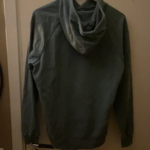 Mörk grön hoodie från Under Armour - Säljer en mörk grön hoodie från Under Armour i bra skick. Den har en mysig huva med dragsko och en praktisk magficka. Perfekt för kyliga dagar eller träning. Passar både till vardags och sportiga aktiviteter. Den passar som S på män.