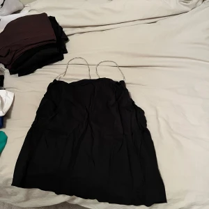 Svart linne med tunna axelband - Säljer en elegant svart linne från H&M med tunna axelband. Perfekt för festliga tillfällen! Linnet har en enkel och stilren design som passar till många olika accessoarer. Den är i bra skick och redo för nya äventyr.