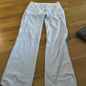 Vita mjukisbyxor med broderad logga - Säljer ett par vita mjukisbyxor i mycket bra skick. De har en broderad logga på framsidan och praktiska fickor med knappar bak. Perfekta för en avslappnad stil och bekväma att bära. Passar till både vardag och mysiga hemmakvällar.