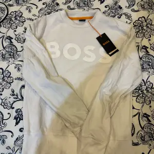 Säljer en snygg vit sweatshirt från BOSS i storlek XS. Tröjan har en stor BOSS-logga på framsidan och är i nytt skick med etikett kvar. Perfekt för en stilren och avslappnad look. Passar både till vardags och fest! Köpt för 1,099kr på zalando, ej använt.