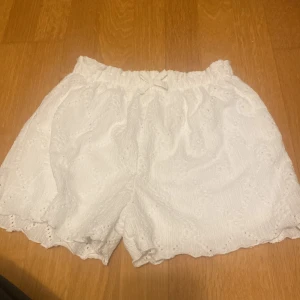 Vita shorts med spetsdetaljer - Säljer ett par supergulliga vita shorts med spetsdetaljer. De är perfekta för sommaren och har en bekväm, loose passform. Materialet känns lätt och luftigt, vilket gör dem idealiska för varma dagar. Passar perfekt till en avslappnad dag på stranden eller en somrig utflykt. 🏖️