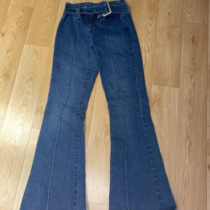 Blå bootcut jeans från FB sisters - Säljer ett par snygga blå bootcut jeans från FB Sister i storlek S. De är lågmidjade och har en klassisk jeanslook med dragkedja och knappar.