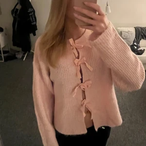 Rosa stickad kofta med knyt - Superfin rosa stickad kofta med knyt framtill. Den är perfekt för både mysiga hemmakvällar och en dag på stan. Koftan har en loose passform och långa ärmar, vilket gör den extra bekväm och stilren. Ett måste i garderoben för alla som älskar en söt och avslappnad stil! 💖