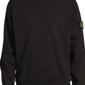 Svart sweatshirt från Stone Island - Säljer en stilren svart sweatshirt från Stone Island. Den har en klassisk design med rund hals och långa ärmar. Perfekt för både vardag och fest. Märkets ikoniska patch finns på ärmen.