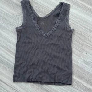 Grå ribbad linne med spetsdetaljer - Säljer en snygg grå ribbad linne från Brandy Melville.. Den har v-ringad hals och ärmlös design med fina spetsdetaljer runt halsen. I mycket bra skick!💝