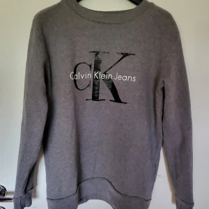 Grå sweatshirt från Calvin Klein Jeans - Säljer en snygg och bekväm grå sweatshirt från Calvin Klein Jeans. Tröjan har en klassisk design med Calvin Klein-loggan tryckt på framsidan. Den är perfekt för både vardag och avslappnade tillfällen. Tröjan är i storlek S och är i mycket bra skick.