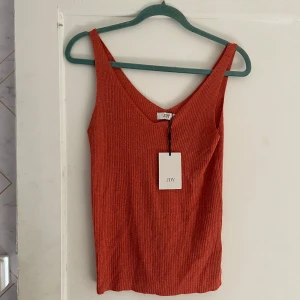 Orange ribbad linnetopp från JDY - Säljer en snygg orange ribbad linnetopp från JDY. Toppen är ärmlös och har en v-ringad hals. Perfekt för sommaren eller en festlig kväll. Helt ny med tag kvar!