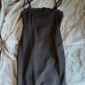 Svart klänning med spetsdetaljer - en elegant svart klänning med spetsdetalj längs överkanten. Klänningen har en tight passform och är perfekt för festliga tillfällen. bra skick!❤️