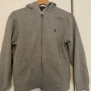 Polo Ralph lauren zip - Det är en grå polo Ralph lauren zip Hoodie som är använd ett fler tal gånger. Men den är jätte bra skick utan hål. Pris kan diskuteras 