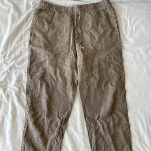 Beige linnebyxor från H&M - Säljer ett par riktigt bekväma beige linnebyxor från H&M i storlek S. Byxorna har en elastisk midja med snörning för extra komfort. Perfekta för en avslappnad stil under varma dagar. De är i regular fit och passar bra till både vardag och sommaraktiviteter.
