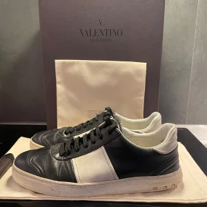 Valentino Flycrew (42) - Säljer ett par snygga svartvita Flycrews från Valentino Garavani. De har en klassisk look som passar perfekt till både vardag och fest. Tillkommer gör box, 2st dustbags och extra fräscha snören. Skorna saknar tyvärr 5 nitar (3 på ena och 2 på andra).