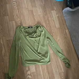 Grön långärmad topp från BikBok - Säljer en snygg grön långärmad topp från BikBok. Toppen har en lös passform och en draperad halsringning som ger en elegant touch. Perfekt för både vardag och fest!